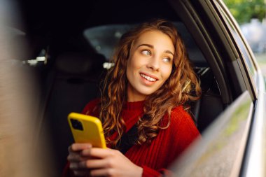 Genç bir kadın arabanın arka koltuğunda oturur ve telefonda konuşur. İş, teknoloji, seyahat, online iletişim kavramı. Taksi..