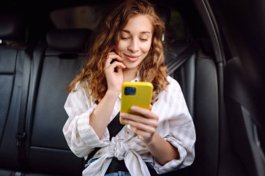 Bir arabanın arka koltuğunda elinde akıllı telefonuyla mutlu bir kadın. Teknoloji kavramı, araba ve iş seyahati..