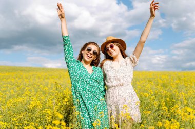 Sarı kolza tohumu tarlasının ortasında iki güzel kadın. Doğa, tatil, rahatlama ve yaşam tarzı. Yaz manzarası.