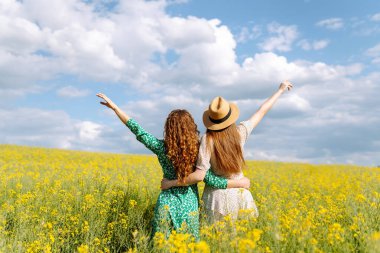 Sarı kolza tohumu tarlasının ortasında iki güzel kadın. Doğa, tatil, rahatlama ve yaşam tarzı. Yaz manzarası.