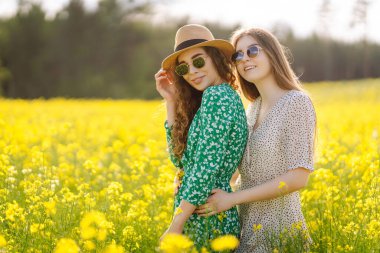 Sarı kolza tohumu tarlasının ortasında iki güzel kadın. Doğa, tatil, rahatlama ve yaşam tarzı. Yaz manzarası.
