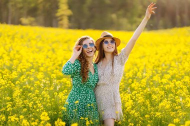 Sarı kolza tohumu tarlasının ortasında iki güzel kadın. Doğa, tatil, rahatlama ve yaşam tarzı. Yaz manzarası.