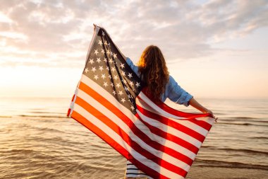 Sahilde elinde ABD bayrağı olan neşeli mutlu kadın eğleniyor. ABD 4 Temmuz 'u kutluyor. Bağımsızlık Günü kavramı