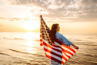 Sahilde elinde ABD bayrağı olan neşeli mutlu kadın eğleniyor. ABD 4 Temmuz 'u kutluyor. Bağımsızlık Günü kavramı