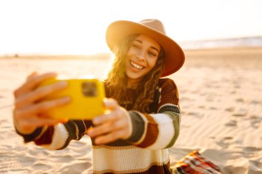 Selfie zamanı. Gün batımında deniz kenarında poz veren güzel kıvırcık kadın. Bahar zamanı. Seyahat, hafta sonu, rahatlama ve yaşam tarzı konsepti..