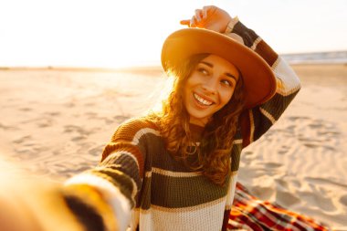 Selfie zamanı. Gün batımında deniz kenarında poz veren güzel kıvırcık kadın. Bahar zamanı. Seyahat, hafta sonu, rahatlama ve yaşam tarzı konsepti..