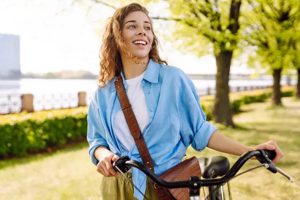 Giovane Donna Sorridente Bicicletta Sul Marciapiede Nel Parco Primaverile Della Immagine Stock