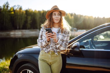 Seyahat sırasında akıllı telefon kullanan mutlu genç kadın sürücü. Seyahat, hafta sonu konsepti.