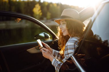 Seyahat sırasında akıllı telefon kullanan mutlu genç kadın sürücü. Seyahat, hafta sonu konsepti.