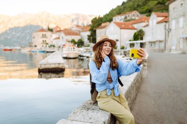 Genç bir kadın sokakta yürüyor ve akıllı telefon kamerasıyla selfie çekiyor. Olumlu anlar kavramı, eğlence. Turizm ve teknoloji
