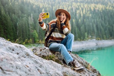 Kadın fotoğraf çekmek için telefon kullanıyor. Dağlarda aile ve arkadaşlar için selfie ve video görüşmeleri yapıyor. Seyahat ve seyahat tutkusu konsepti.