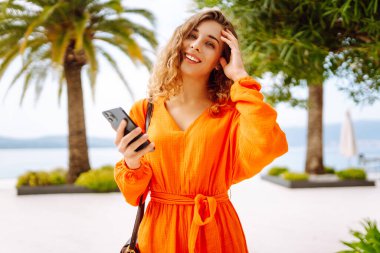 Avrupa şehrinde sokakta akıllı telefon kullanan kendine güvenen genç bir kadın. Seyahat, moda, blog konsepti.