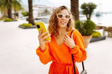 Avrupa şehrinde sokakta akıllı telefon kullanan kendine güvenen genç bir kadın. Seyahat, moda, blog konsepti.