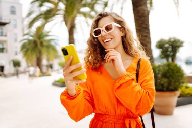 Avrupa şehrinde sokakta akıllı telefon kullanan kendine güvenen genç bir kadın. Seyahat, moda, blog konsepti.