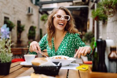 Yazlık kafede oturan genç bir kadın domatesli makarna yiyor, et yiyor. Bolonez. Parmesan peyniri. Seyahat, turizm, yiyecek ve içecek..