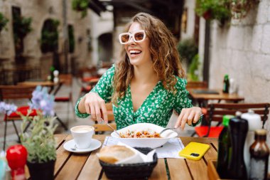 Yazlık kafede oturan genç bir kadın domatesli makarna yiyor, et yiyor. Bolonez. Parmesan peyniri. Seyahat, turizm, yiyecek ve içecek..