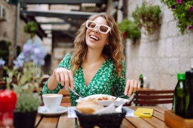 Yazlık kafede oturan genç bir kadın domatesli makarna yiyor, et yiyor. Bolonez. Parmesan peyniri. Seyahat, turizm, yiyecek ve içecek..