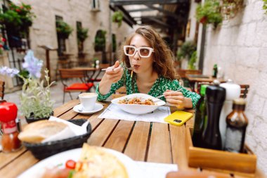 Yazlık kafede oturan genç bir kadın domatesli makarna yiyor, et yiyor. Bolonez. Parmesan peyniri. Seyahat, turizm, yiyecek ve içecek..