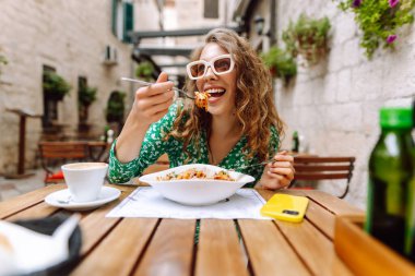 Yazlık kafede oturan genç bir kadın domatesli makarna yiyor, et yiyor. Bolonez. Parmesan peyniri. Seyahat, turizm, yiyecek ve içecek..