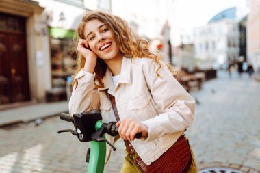 Güneşli bir günde şehrin caddesinde elektrikli scooter süren güzel bir kadın. Ekolojik nakliye. Etkin yaşam biçimi.