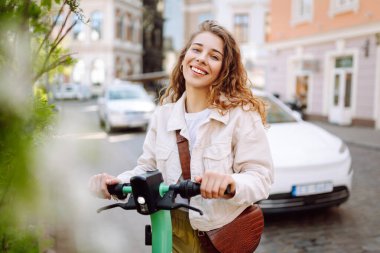 Güneşli bir günde şehrin caddesinde elektrikli scooter süren güzel bir kadın. Ekolojik nakliye. Etkin yaşam biçimi.