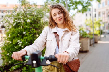 Güneşli bir günde şehrin caddesinde elektrikli scooter süren güzel bir kadın. Ekolojik nakliye. Etkin yaşam biçimi.