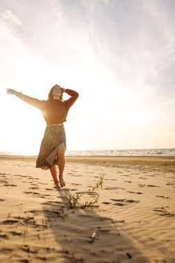 Güzel bir kadın gün batımında güzel bir kumsal boyunca yürür. Seyahat, hafta sonu, rahatlama ve yaşam tarzı konsepti.