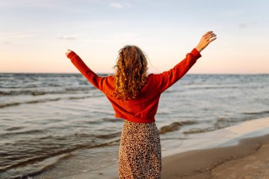 Güzel bir kadın gün batımında güzel bir kumsal boyunca yürür. Seyahat, hafta sonu, rahatlama ve yaşam tarzı konsepti.