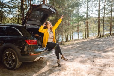 Genç bir kadın bagajda oturmuş doğanın tadını çıkarıyor. Arabayla yolculuk. Yaşam tarzı, seyahat, turizm, doğa konsepti.