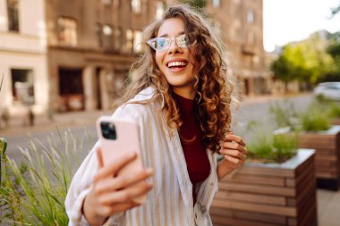 Şehir caddesinde telefonla yürüyen güzel, gülümseyen bir kadın. İş, eğitim, teknoloji, blog, iletişim kavramı.