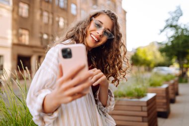Şehir caddesinde telefonla yürüyen güzel, gülümseyen bir kadın. İş, eğitim, teknoloji, blog, iletişim kavramı.