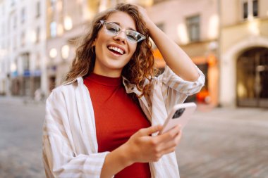 Şehir caddesinde telefonla yürüyen güzel, gülümseyen bir kadın. İş, eğitim, teknoloji, blog, iletişim kavramı.