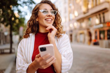 Şehir caddesinde telefonla yürüyen güzel, gülümseyen bir kadın. İş, eğitim, teknoloji, blog, iletişim kavramı.