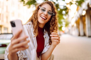 Şehir caddesinde telefonla yürüyen güzel, gülümseyen bir kadın. İş, eğitim, teknoloji, blog, iletişim kavramı.