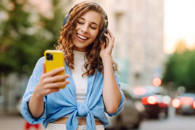 Dans eden, müzik dinleyen, kulaklıklı ve akıllı telefonlu genç bir kadın. Sokak tarzı. Güzellik ve moda. 