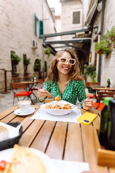 Yazlık kafede oturan genç bir kadın domatesli makarna yiyor, et yiyor. Bolonez. Parmesan peyniri. Seyahat, turizm, yiyecek ve içecek..