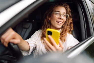 Sürücü koltuğunda oturan genç bir kadın akıllı telefona bakıyor, şehirde park ve gezinti için para ödüyor. Boş zaman, seyahat, teknoloji..
