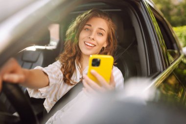 Sürücü koltuğunda oturan genç bir kadın akıllı telefona bakıyor, şehirde park ve gezinti için para ödüyor. Boş zaman, seyahat, teknoloji..