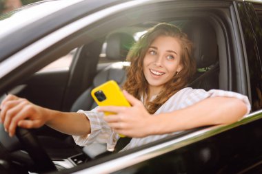 Sürücü koltuğunda oturan genç bir kadın akıllı telefona bakıyor, şehirde park ve gezinti için para ödüyor. Boş zaman, seyahat, teknoloji..