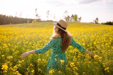 Güzel bir kadın sarı tarla kolza doğru koşar. Doğa, moda, yaz yaşam tarzı.
