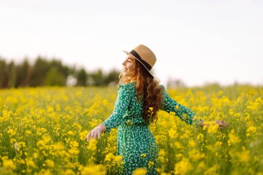 Güzel bir kadın sarı tarla kolza doğru koşar. Doğa, moda, yaz yaşam tarzı.