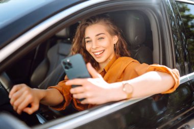 Araba kullanırken akıllı telefonuyla mesaj atan genç bir kadın. Araba paylaşımı, kiralama servisi ya da taksi uygulaması. Yaşam tarzı, seyahat, turizm, aktif yaşam.