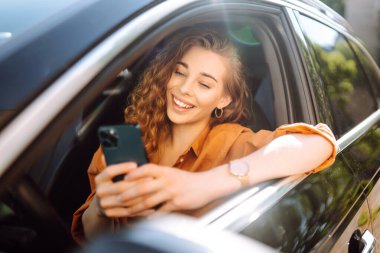 Araba kullanırken akıllı telefonuyla mesaj atan genç bir kadın. Araba paylaşımı, kiralama servisi ya da taksi uygulaması. Yaşam tarzı, seyahat, turizm, aktif yaşam.