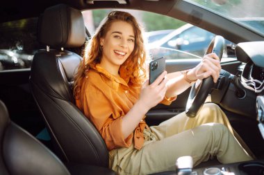 Araba kullanırken akıllı telefonuyla mesaj atan genç bir kadın. Araba paylaşımı, kiralama servisi ya da taksi uygulaması. Yaşam tarzı, seyahat, turizm, aktif yaşam.