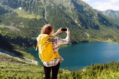 Turist kadın, uçurumun tepesinde, vadi manzaralı bir selfie çekiyor. Seyahat macerasını paylaşıyor. Yaşam tarzı, seyahat, turizm, aktif yaşam.