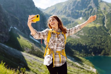 Turist kadın, uçurumun tepesinde, vadi manzaralı bir selfie çekiyor. Seyahat macerasını paylaşıyor. Yaşam tarzı, seyahat, turizm, aktif yaşam.