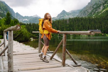 Sarı sırt çantası ve yürüyüş çubuklarıyla gezen kadın gezgin manzaranın tadını çıkarıyor. Aktif yaşam tarzı. Seyahat tutkusu.