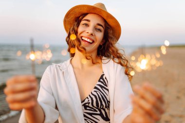 Kumsaldaki genç bayanın ellerindeki maytaplar. Kumsalda havai fişeklerle eğlenen mutlu kadın. Yaz tatili, tatil, rahatlama ve yaşam tarzı konsepti.