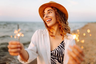 Kumsaldaki genç bayanın ellerindeki maytaplar. Kumsalda havai fişeklerle eğlenen mutlu kadın. Yaz tatili, tatil, rahatlama ve yaşam tarzı konsepti.