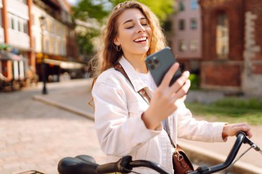 Bisiklet, kadın ve telefon şehirde heyecanlı ve mutlu bir şekilde yazları açık havada modaya uygun bir şekilde mesajlaşırken. Seyahat, hafta sonu, rahatlama ve yaşam tarzı konsepti. 